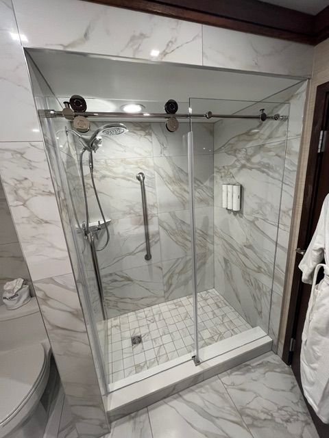 Modern bathroom with glass walk-in shower, marble tile walls and floor, and a handheld showerhead.