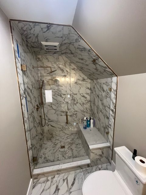 Marble-tiled shower with glass enclosure, built-in bench, and toilet in a small bathroom