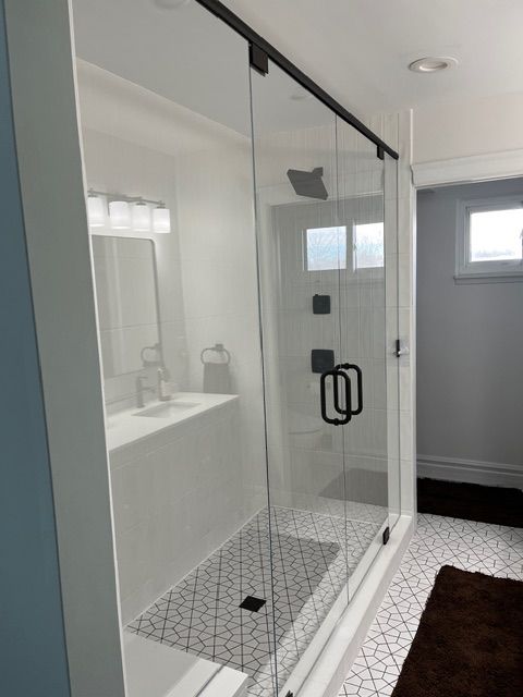Modern bathroom with glass shower enclosure, white tile, and black geometric shower floor.