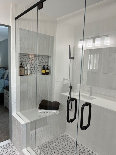 Modern shower with clear glass doors, black handles, built-in shelf, and patterned tile floor.