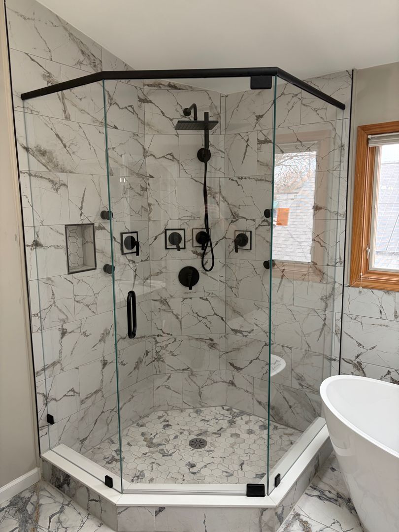 Corner glass shower with marble-look tile, black trim, and built-in controls in a bathroom