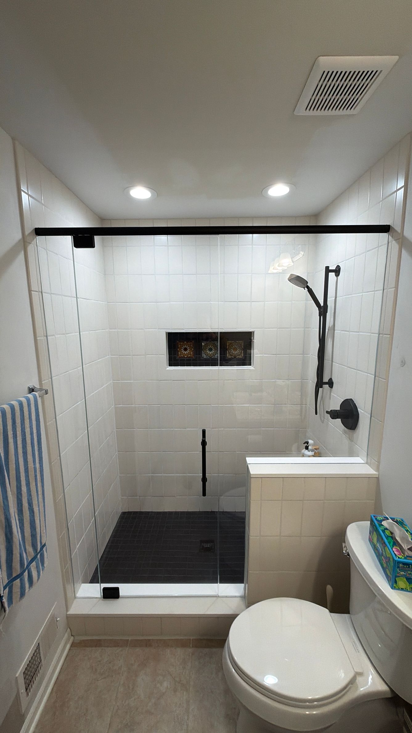 Walk-in shower with white tile, black floor mat, handheld showerhead, and toilet in a small bathroom
