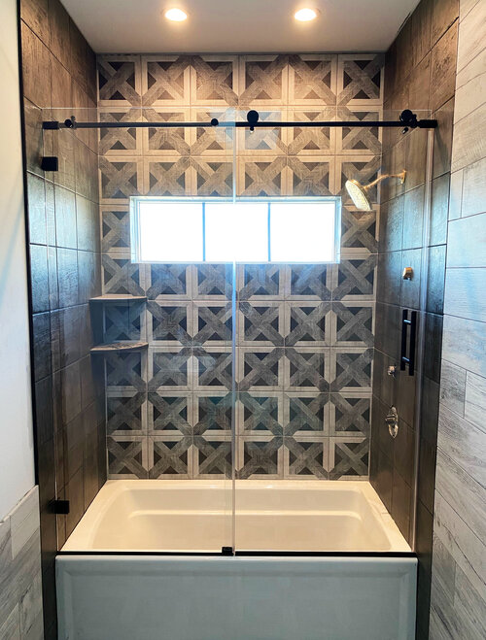 Modern tiled shower with glass enclosure, sliding black shower rod, and frosted window above a white tub.