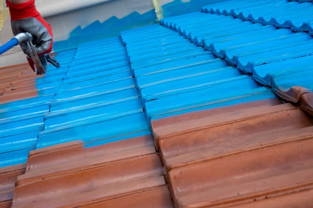Person spraying blue paint on a terracotta tile roof — Geoff Hall Roofing in Port Macquarie, NSW