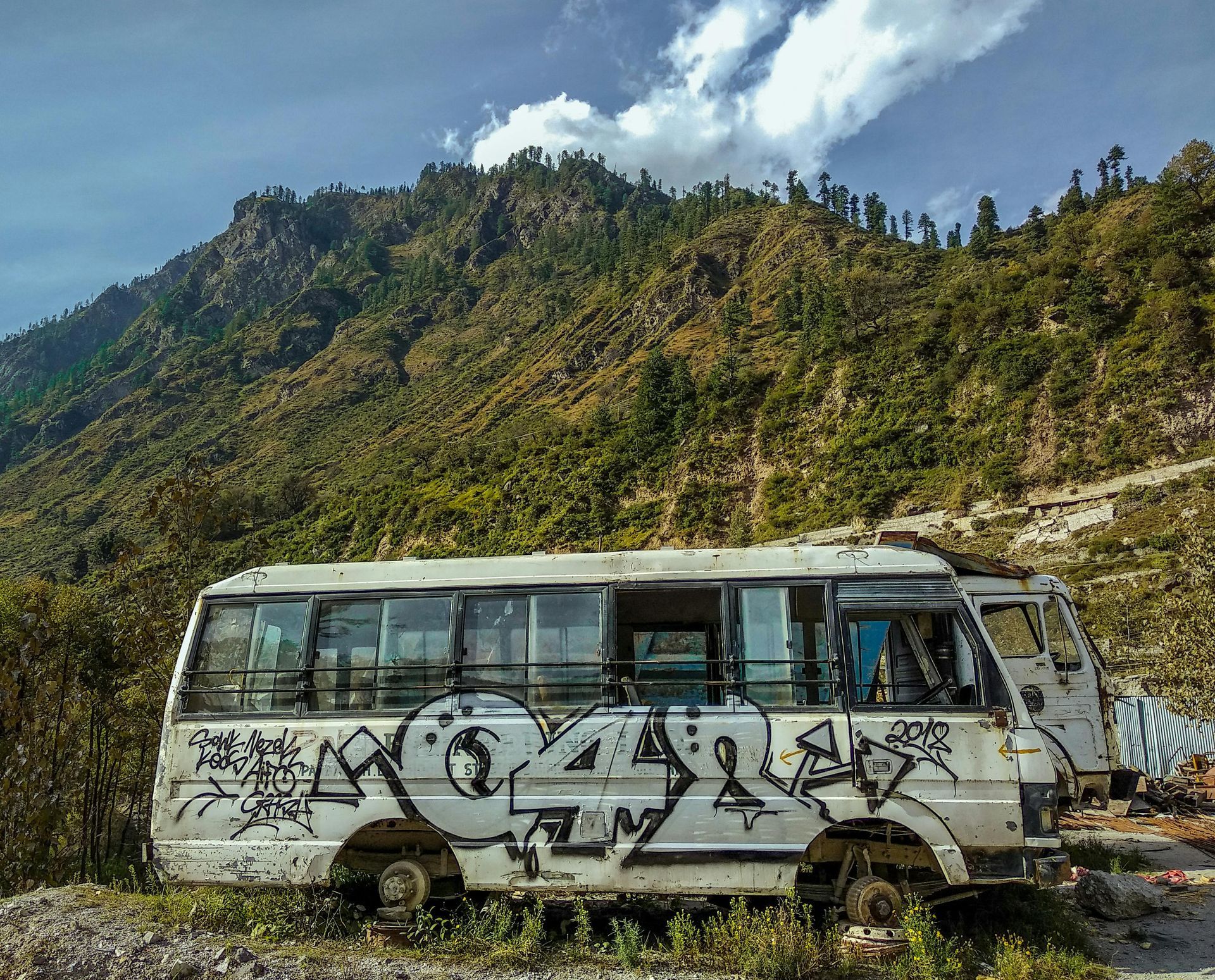 A white bus with graffiti on it is parked in front of a mountain.