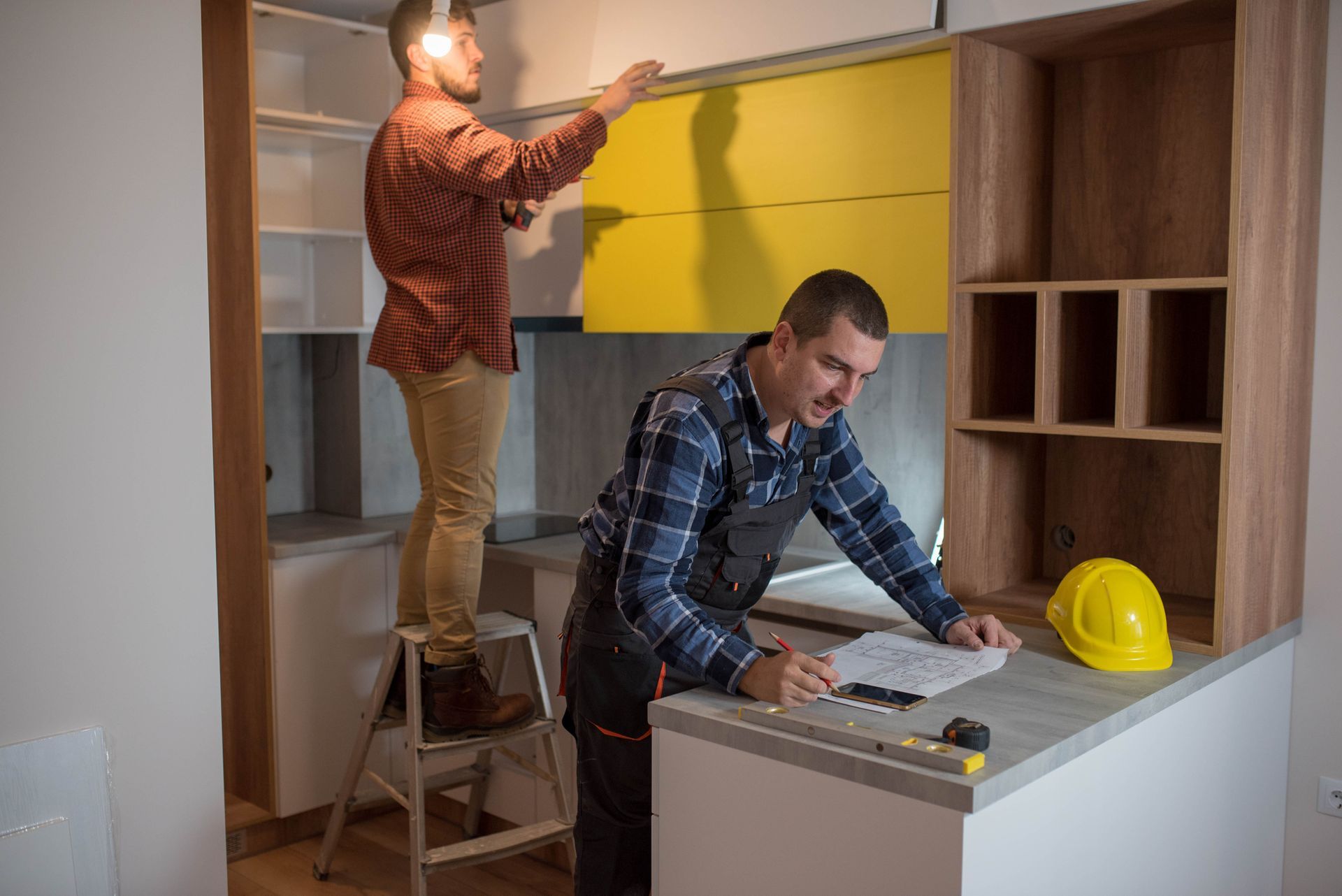 Two men are assembling a kitchen cabinet in a workshop as part of a kitchen renovation project.