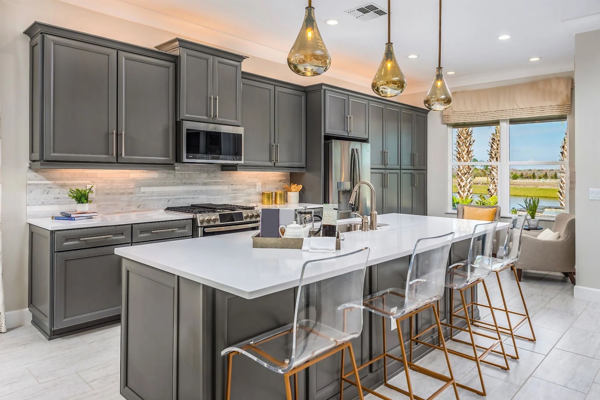 Gray kitchen with island, white countertops, clear bar stools, and gold pendant lights.
