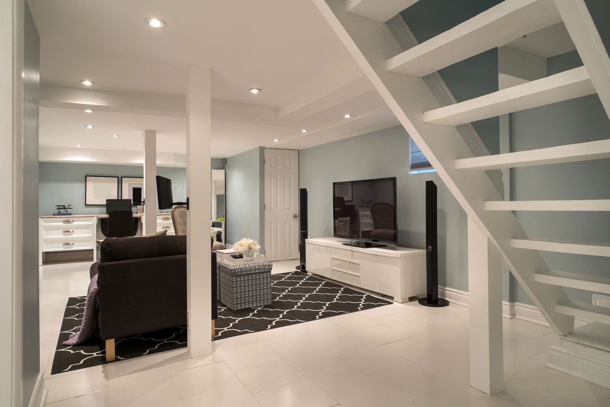 A living room in a basement with stairs and a flat screen tv