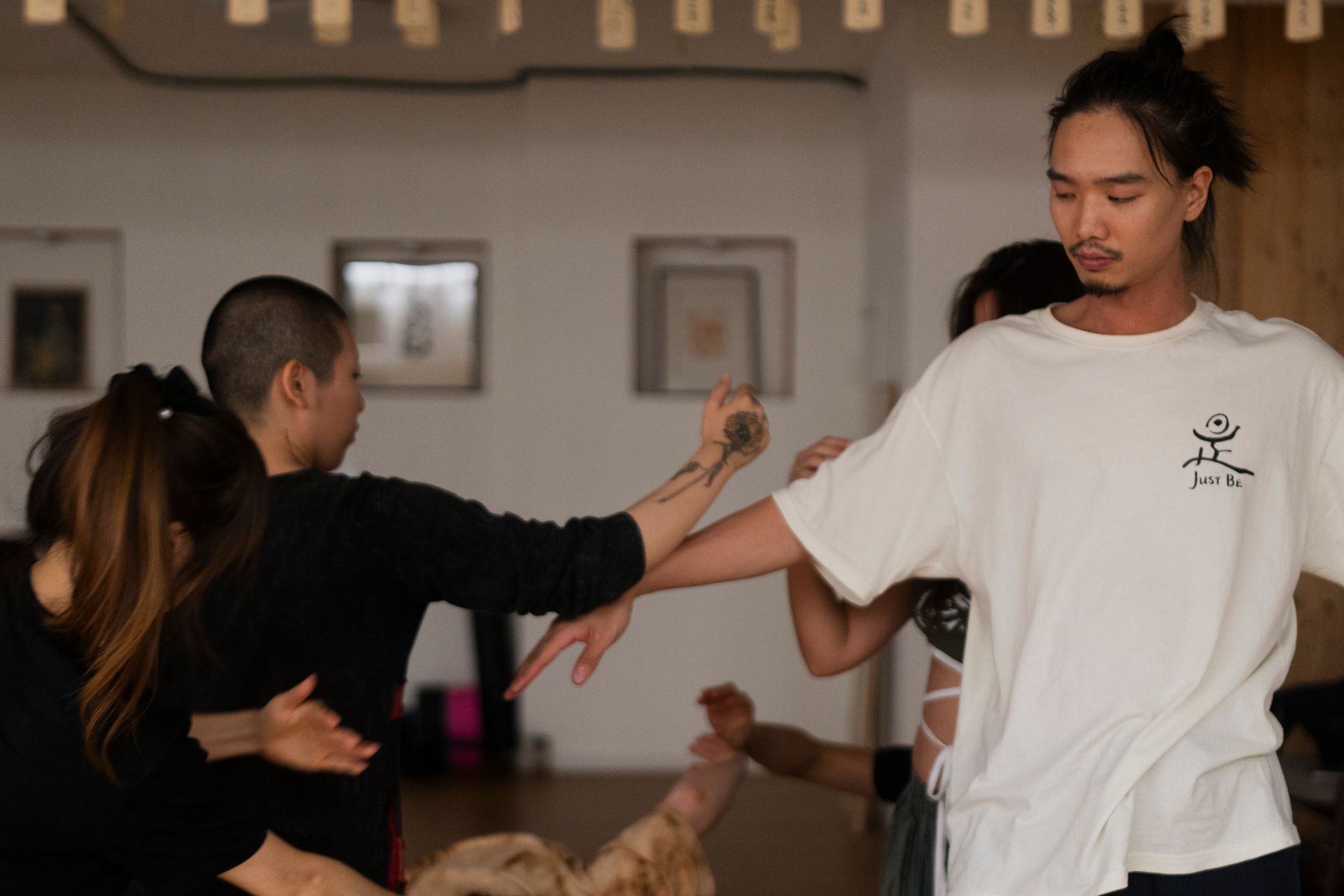 People in a dance class, practicing movements. The instructor, wearing a white shirt, guides the group.