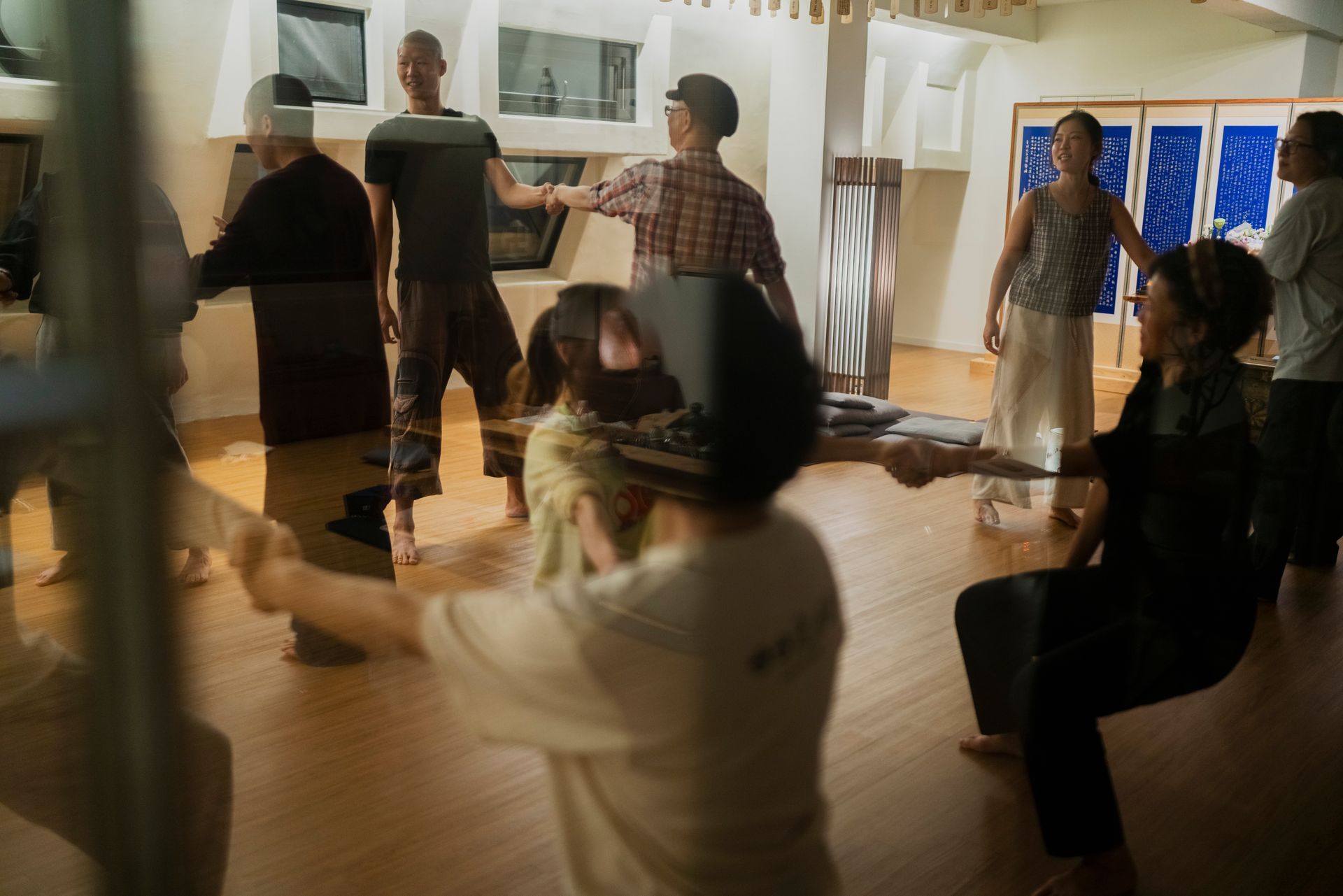 People in a brightly lit room dancing, some holding hands. Hardwood floor.