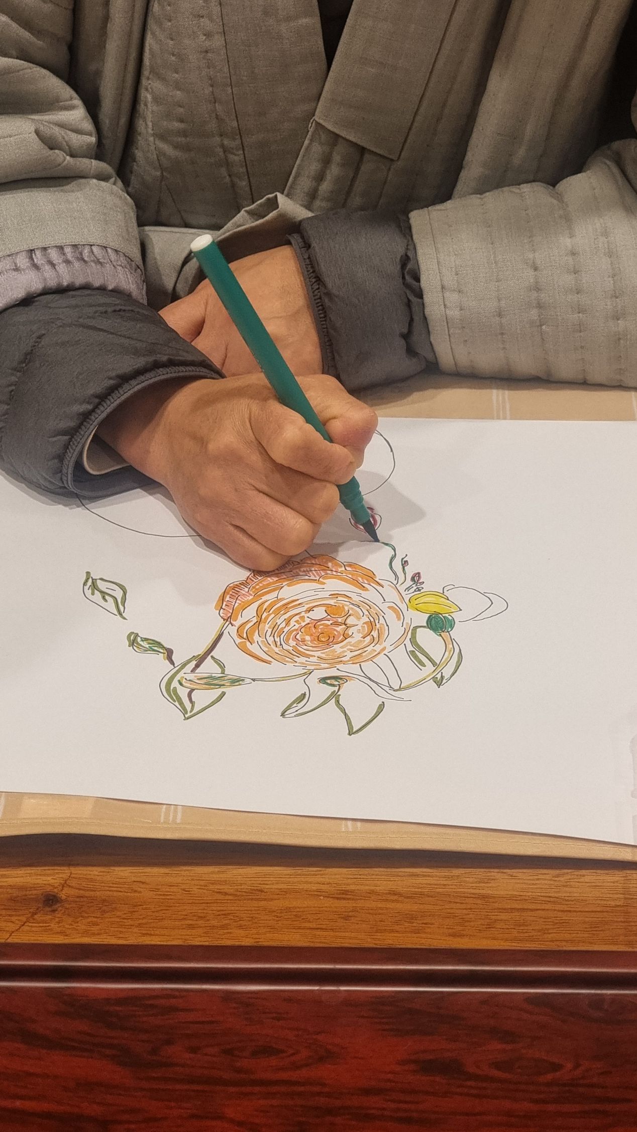 A person is drawing a flower with a green marker on white paper.