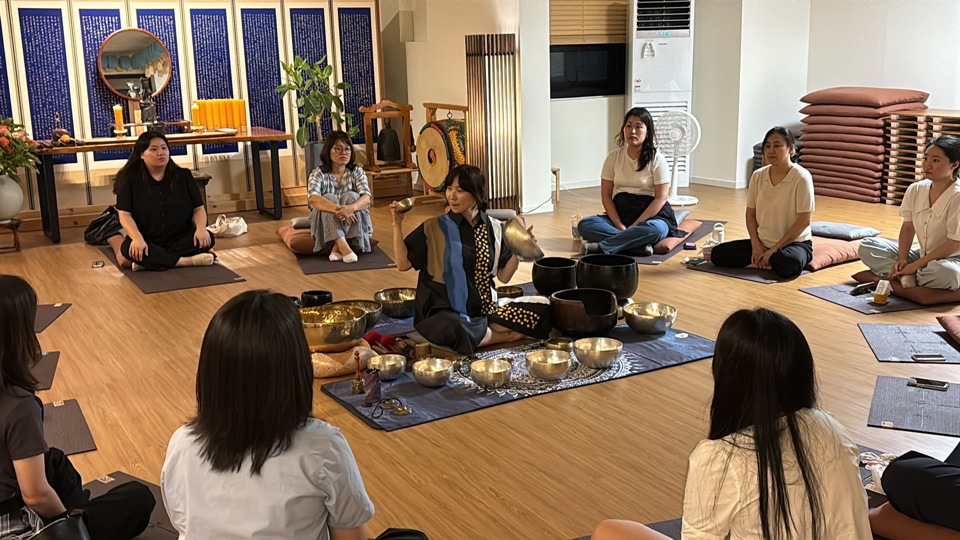 사운드 힐링 세션: 여성 몇 명이 원을 그리며 앉아 사운드 볼을 연주하는 사람의 연주를 듣는 세션입니다.