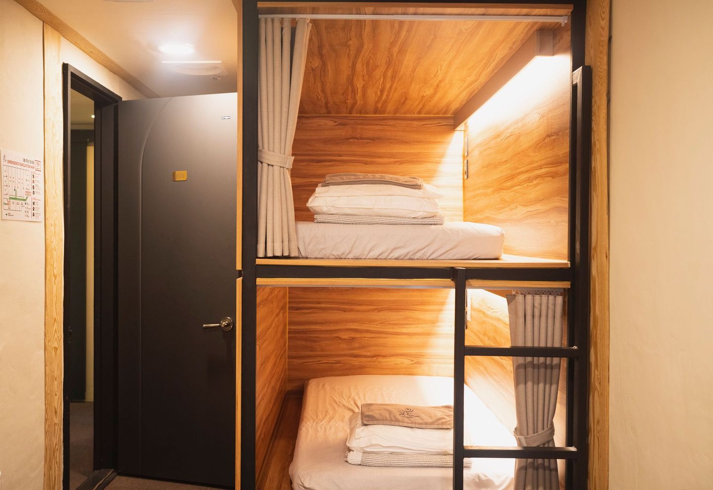 Bunk beds in a wood-paneled capsule hotel room. Black frame with curtains and a ladder.