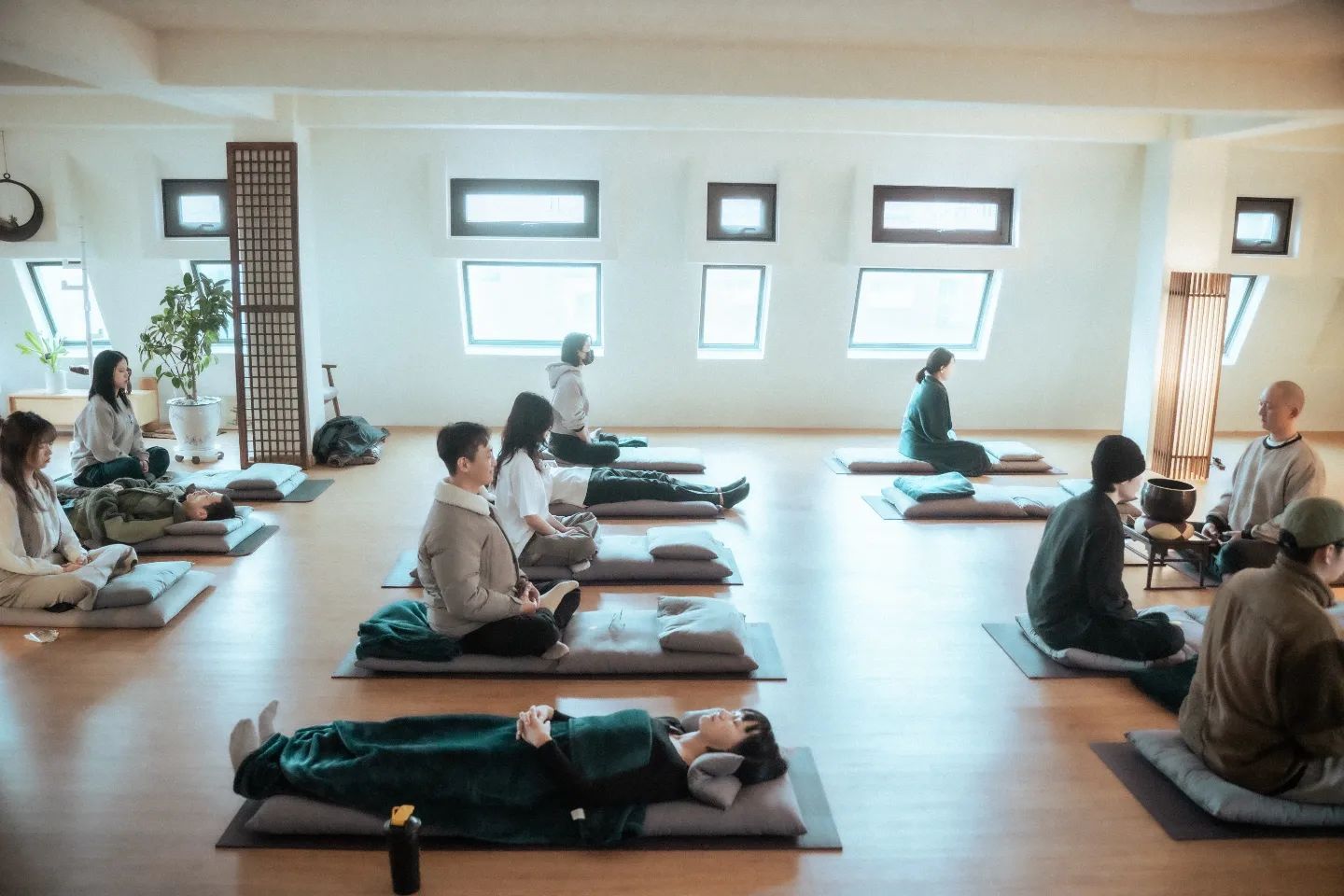 People in a meditation room, sitting or lying on cushions, practicing mindfulness.