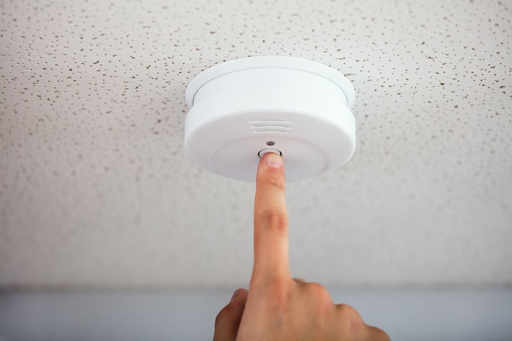 Person Testing a White Smoke Detector — EBS NQ Electronic Building Systems in Kirwan, QLD