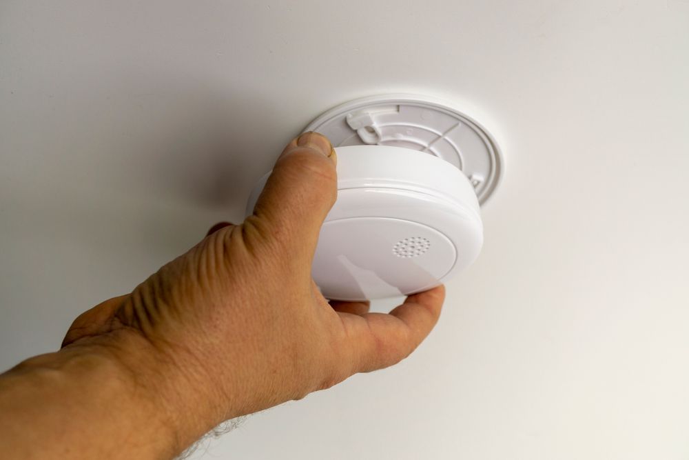 Hand Installing a White Smoke Detector on a White Ceiling — EBS NQ Electronic Building Systems in Kirwan, QLD