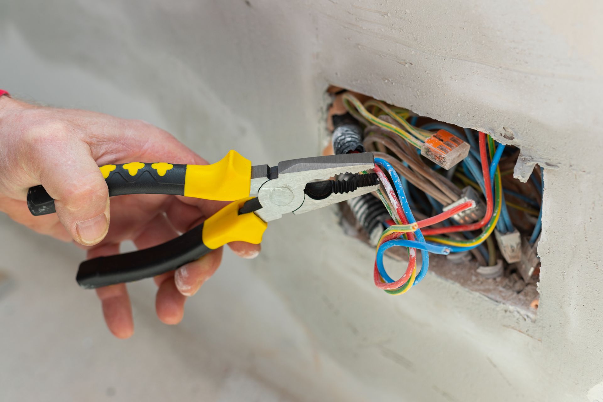 Hand With Pliers Working on Electrical Wiring Inside a Wall — EBS NQ Electronic Building Systems in Kirwan, QLD