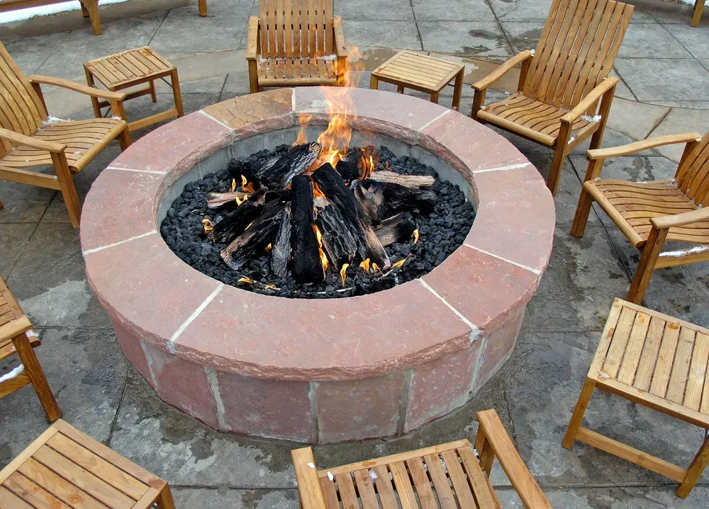 A lit fire pit surrounded by wooden chairs on a patio.