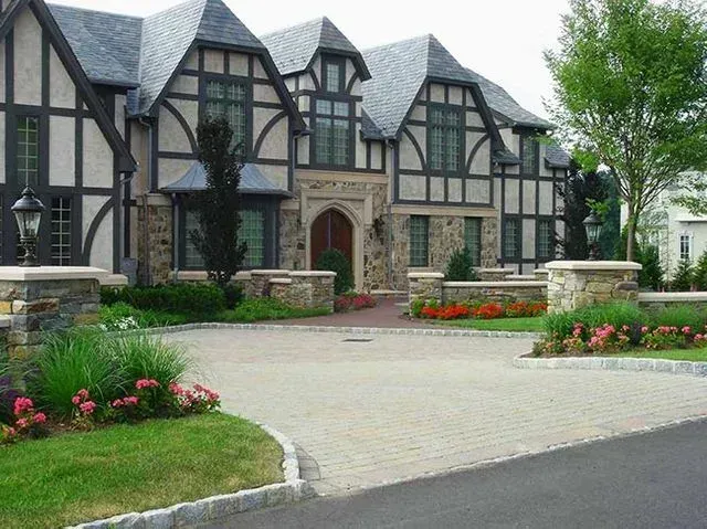 Tudor-style house with brick driveway, stone accents, and manicured landscaping.