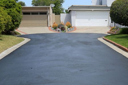Paved driveway leading to two garages, flanked by green lawns.
