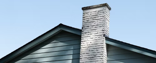Chimney extending from a blue-green house roof against a clear sky.