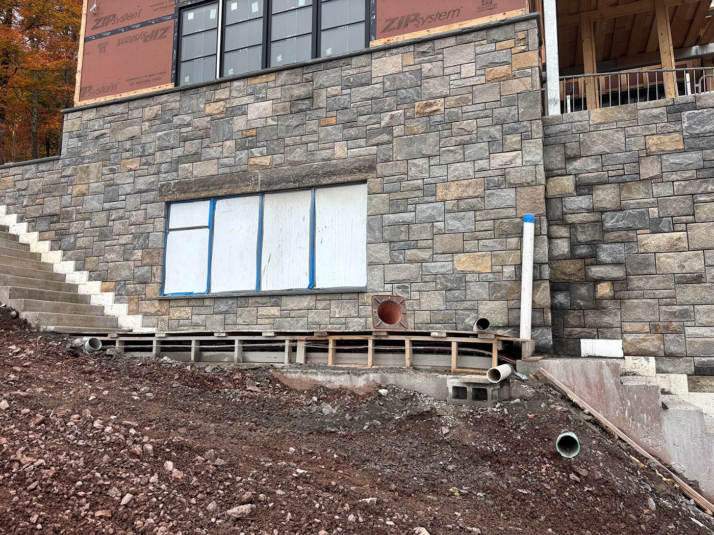 Stone facade under construction on a hillside, with a window and wooden framework.