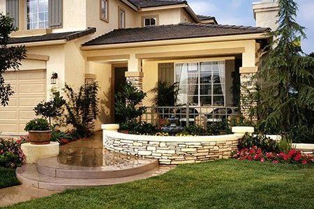 Tan house with stone and brick details, front porch, and green lawn.