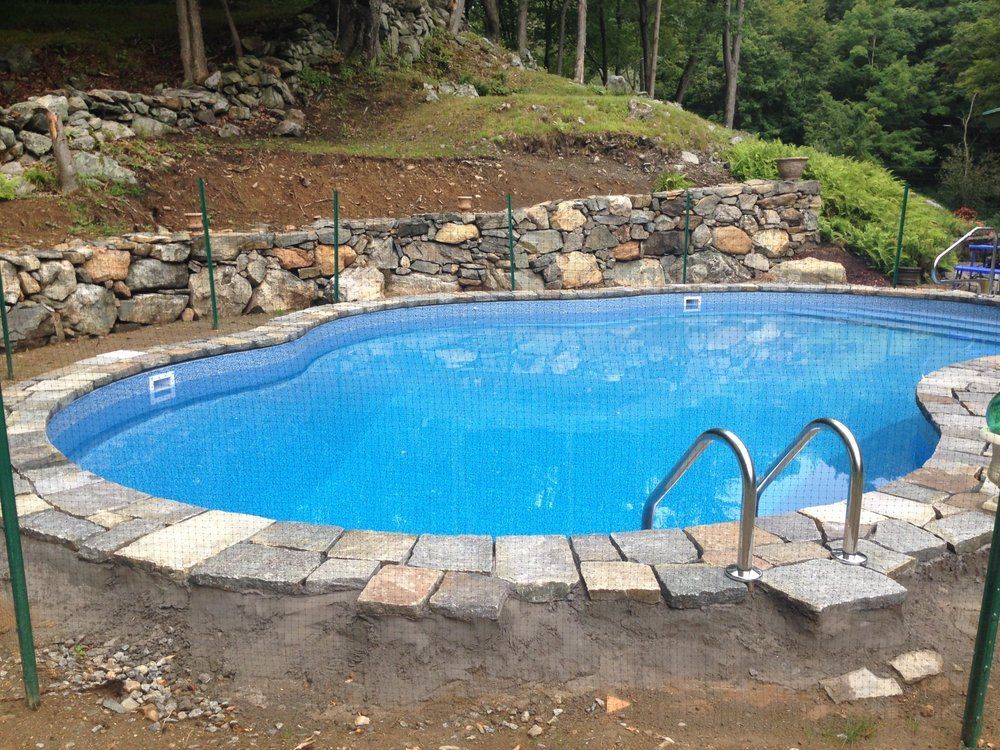 Swimming pool with stone border, retaining wall, and green supports in a backyard setting.