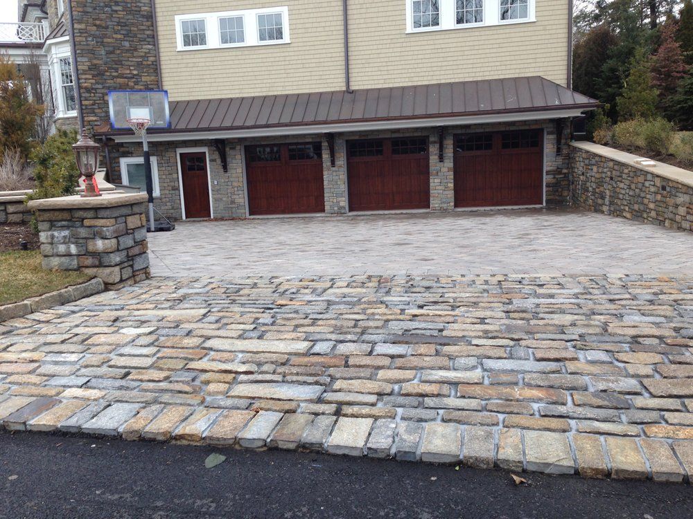 Stone driveway leading to a three-car garage with red doors and basketball hoop.