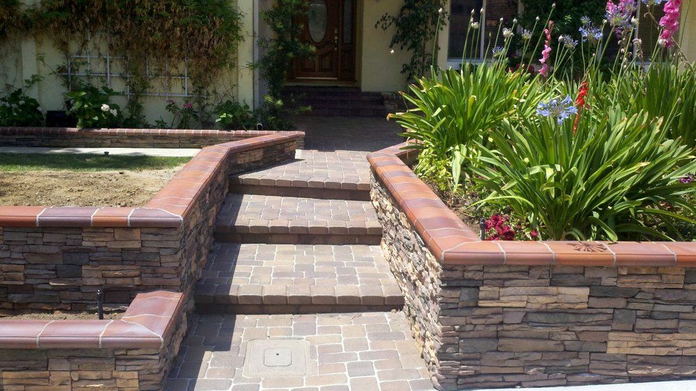 Brick pathway and steps leading to a house entrance, flanked by brick retaining walls and landscaping.