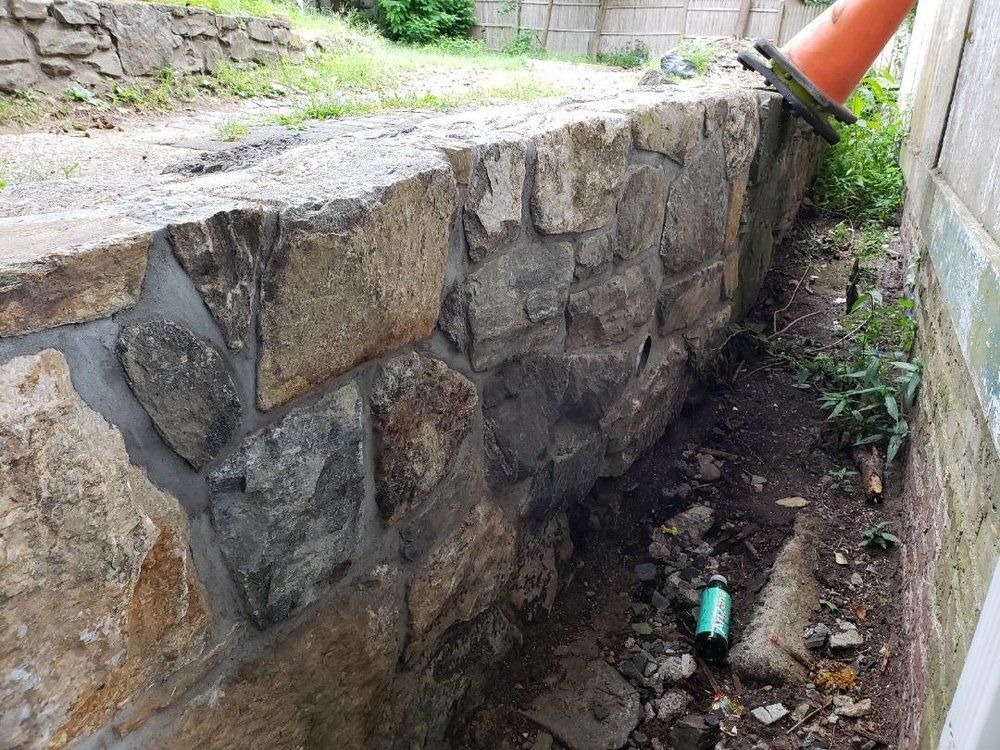 Stone retaining wall beside a building with an orange cone and dirt.