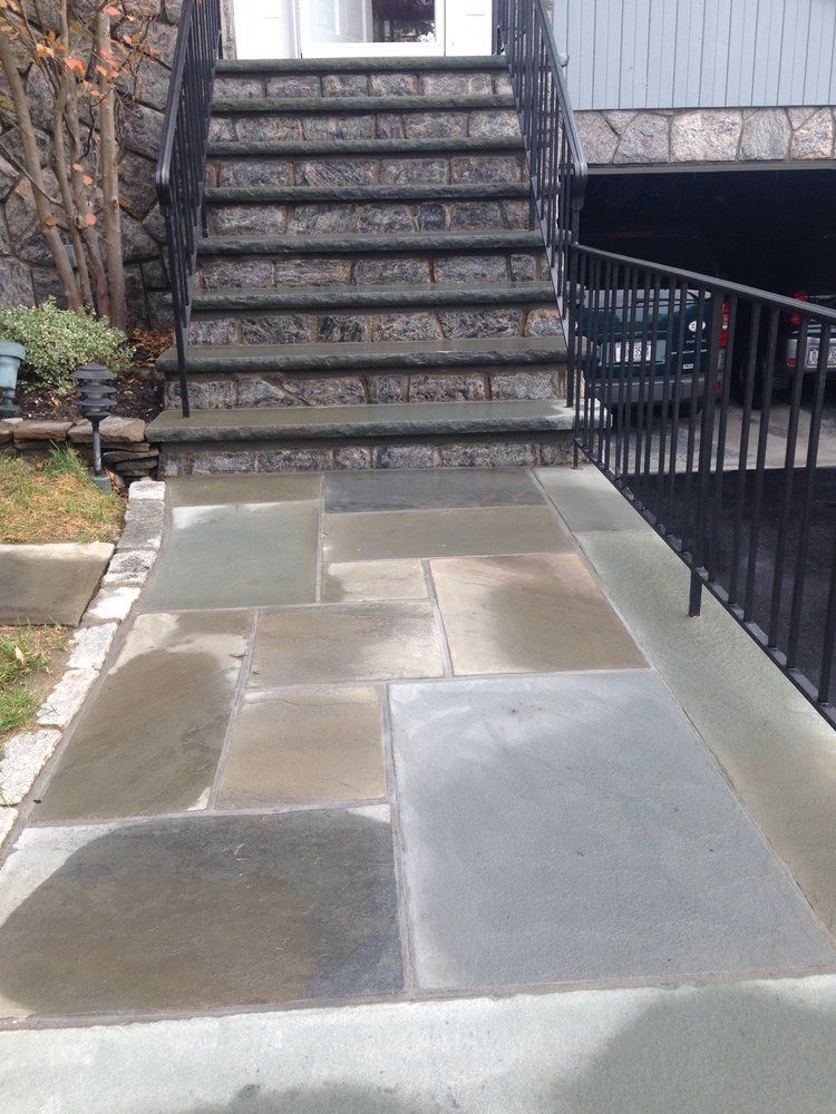 Stone walkway leading to front steps and a house with a black railing, overcast day.