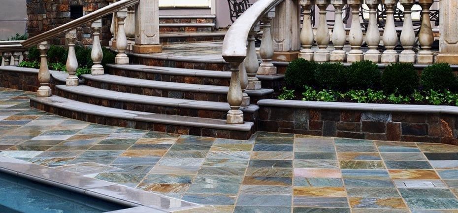 Stone patio with steps and balustrade next to a pool.