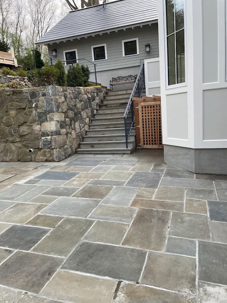 Stone patio and stairs lead up to a gray house, with stone retaining wall.