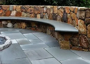 Curved stone bench along a rock wall beside a paved patio area