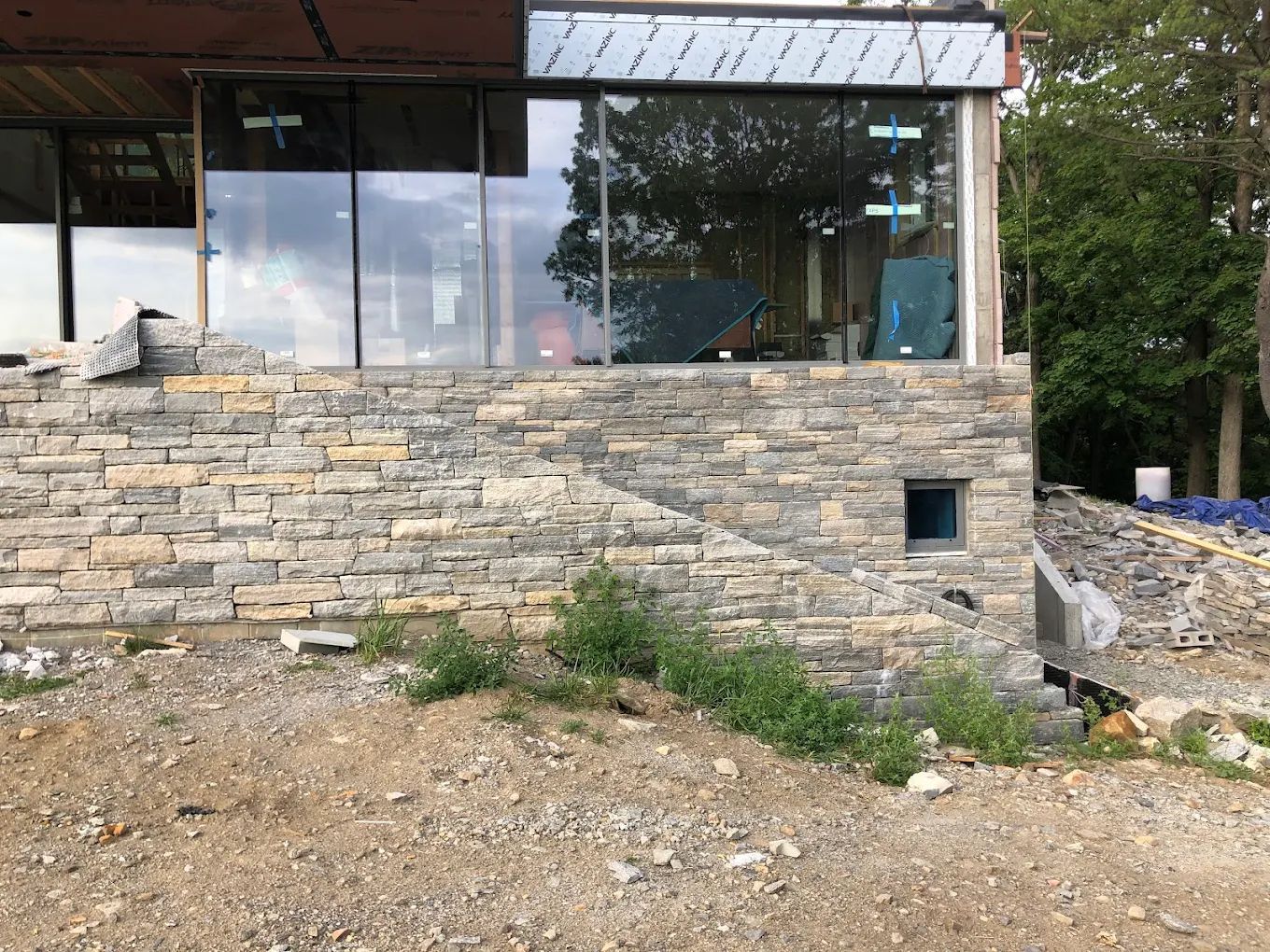 Stone facade of a building under construction, with large glass windows and unfinished surroundings.