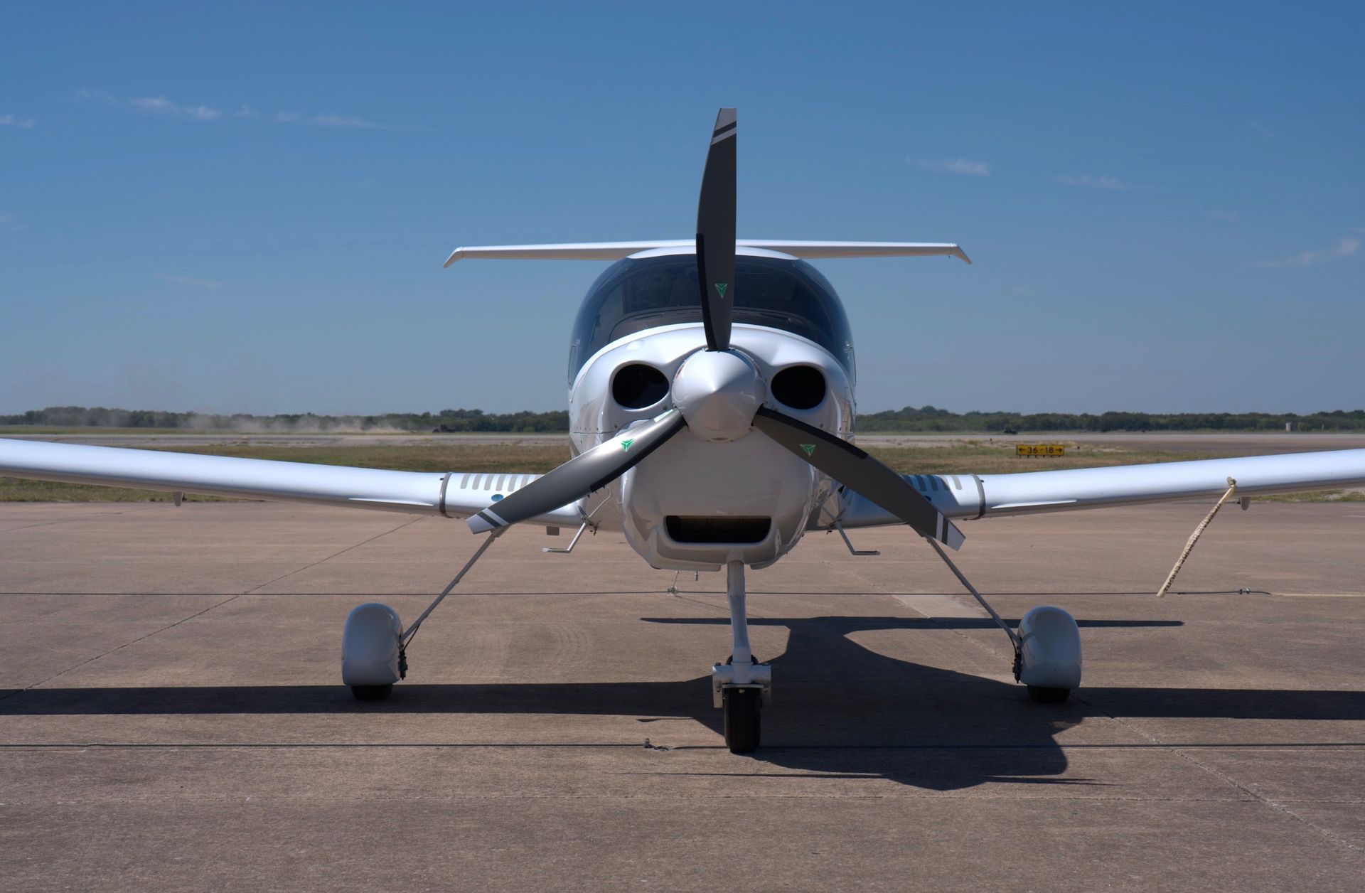White airplane on a runway, propeller in front. Clear blue sky in the background.