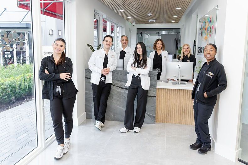 Seven people standing in a bright lobby, dressed in black and white uniforms, near a reception counter