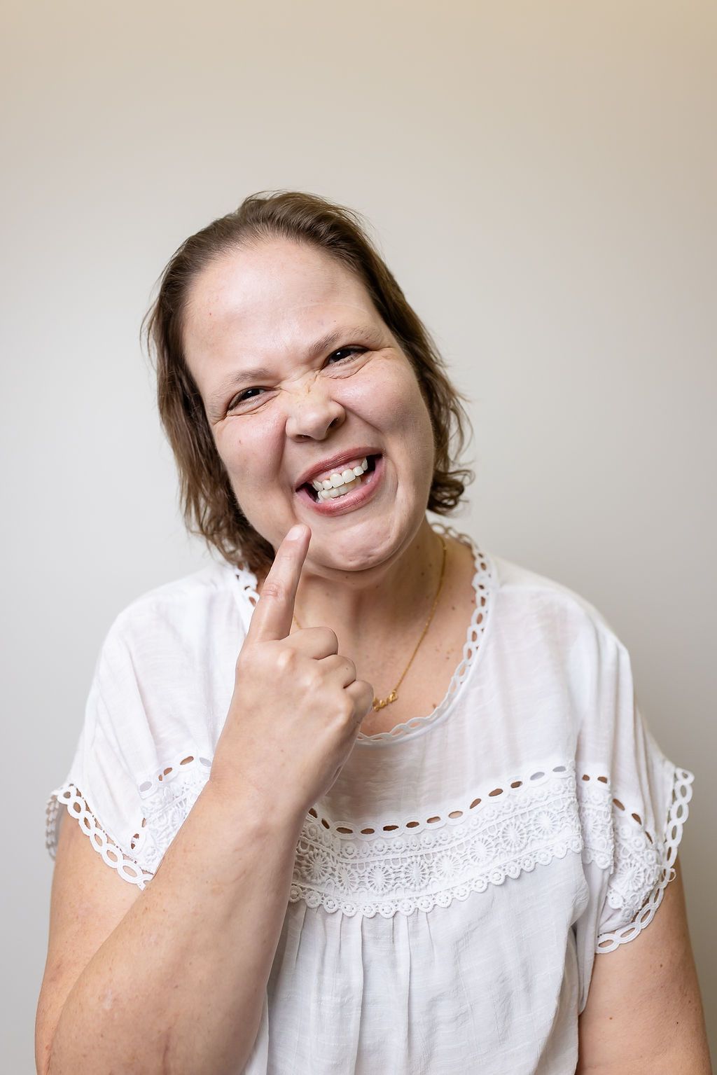 Woman in a white blouse touching a tooth and smiling