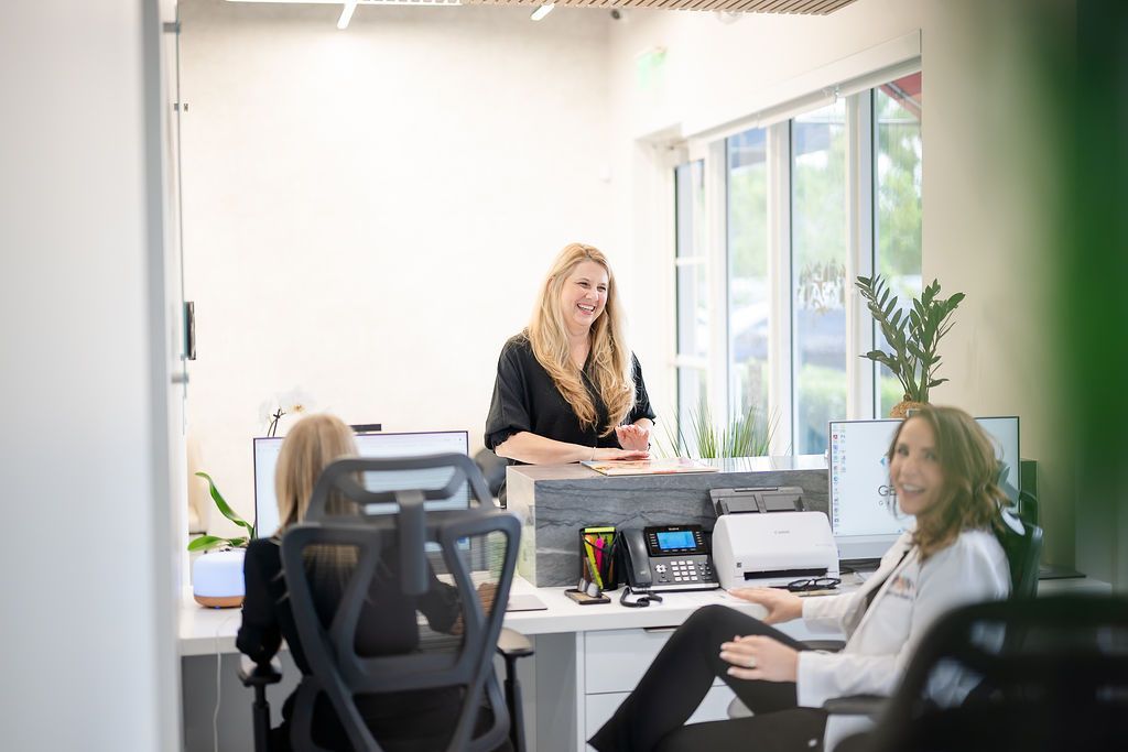 Reception desk in a bright dental office, with staff greeting two visitors and a “GDN dentistry” sign nearby