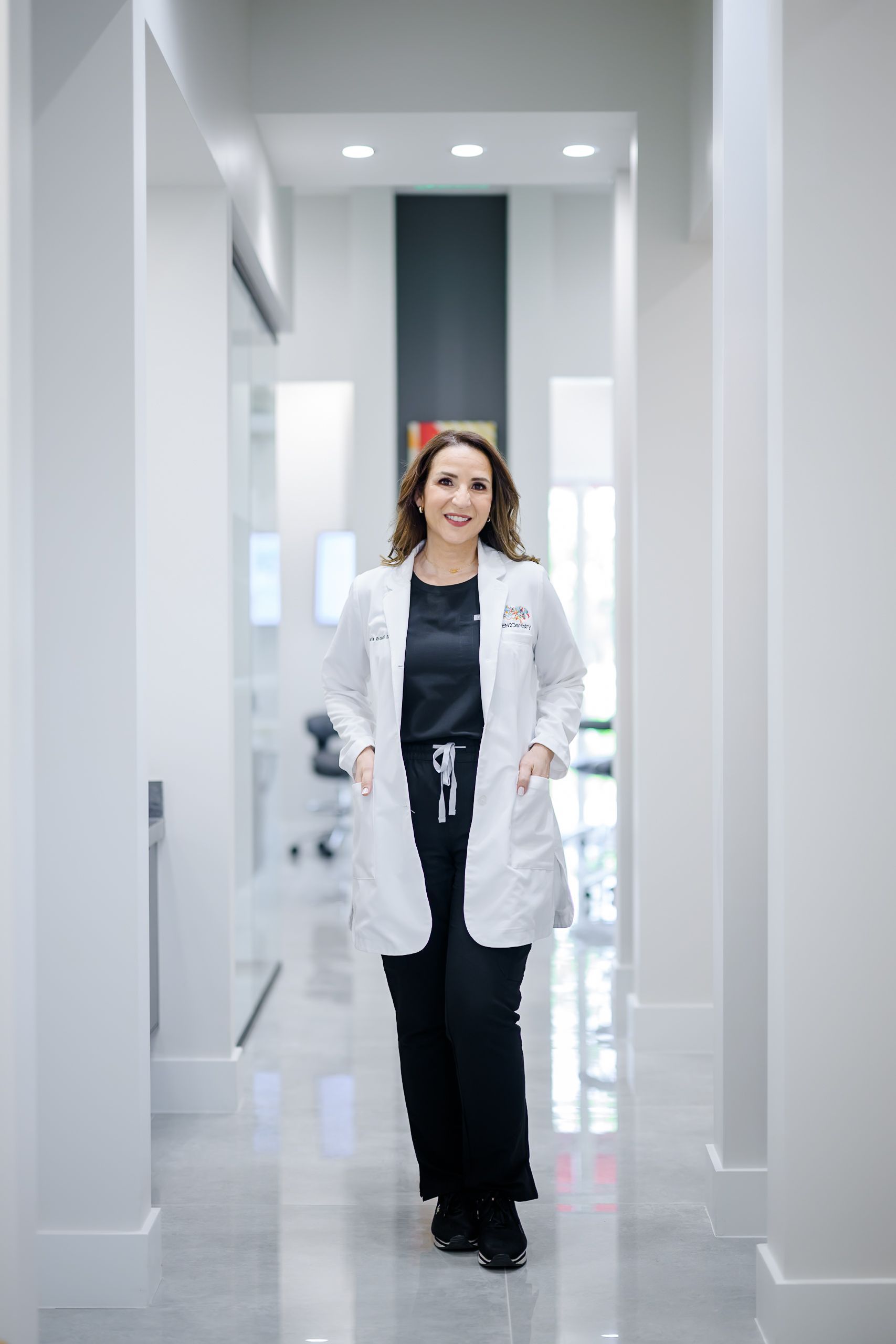 Woman in a white lab coat walking down a bright hallway in a modern clinic