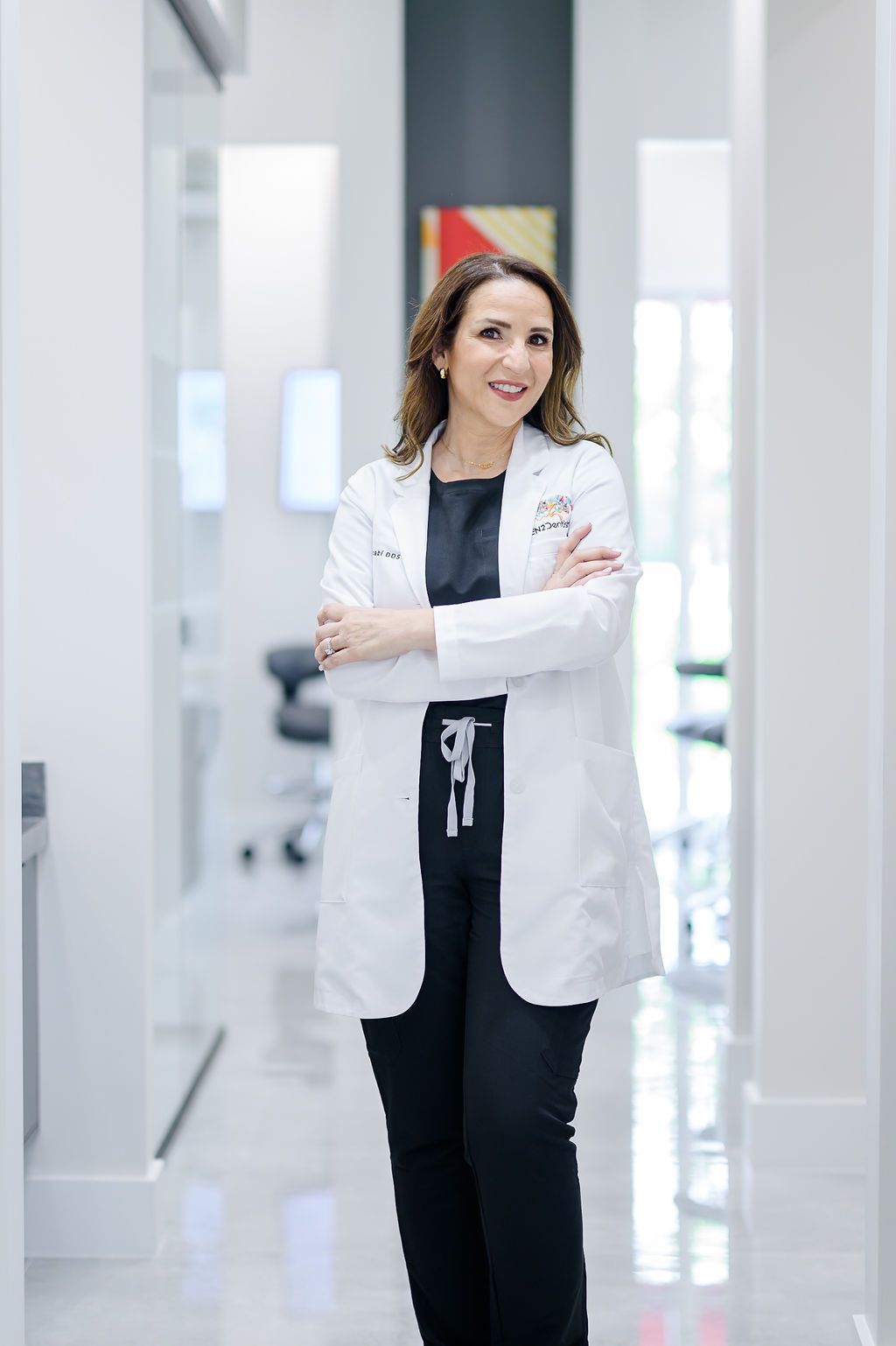 Smiling doctor in a white coat standing with arms crossed in a bright hospital corridor
