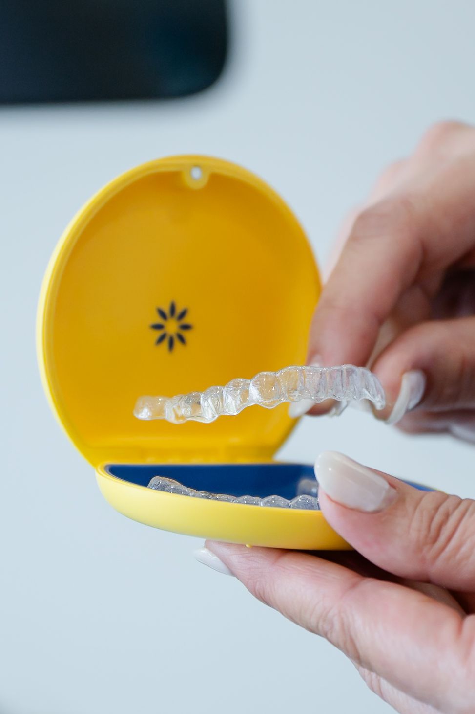 Hand holding a clear dental aligner in a yellow case with blue lining