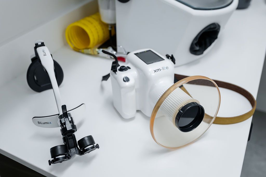 Handheld dental X-ray unit beside magnifying loupes on a clinic counter