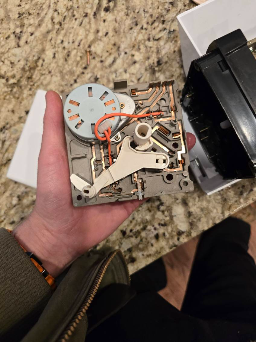 Hand holding a small appliance timer with exposed circuits and mechanical components.