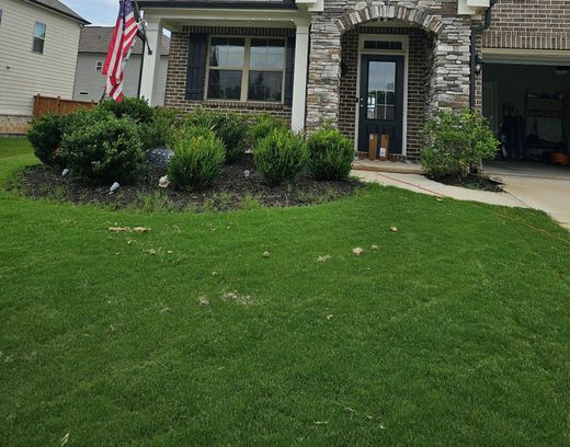 Front yard of a stone house with green lawn, shrubs, and a walkway to the front door.