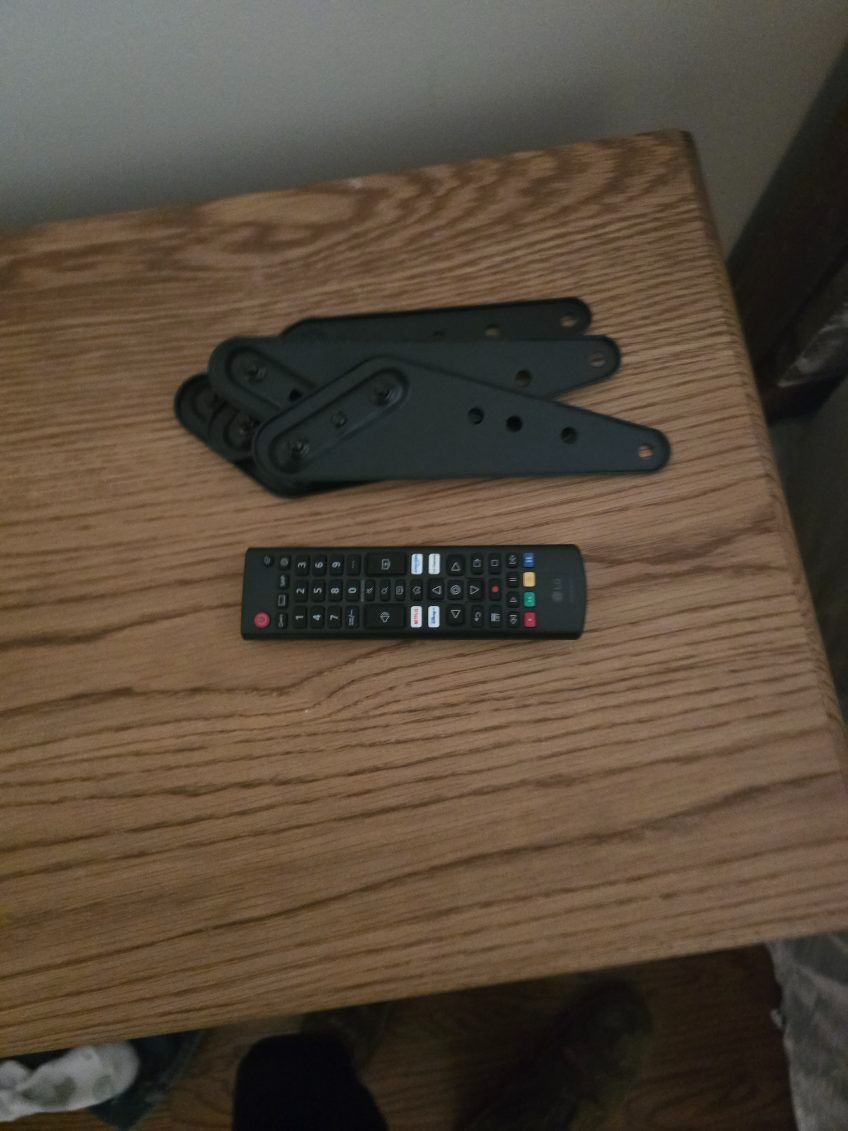 Black plastic brackets and TV remote on a wooden table.