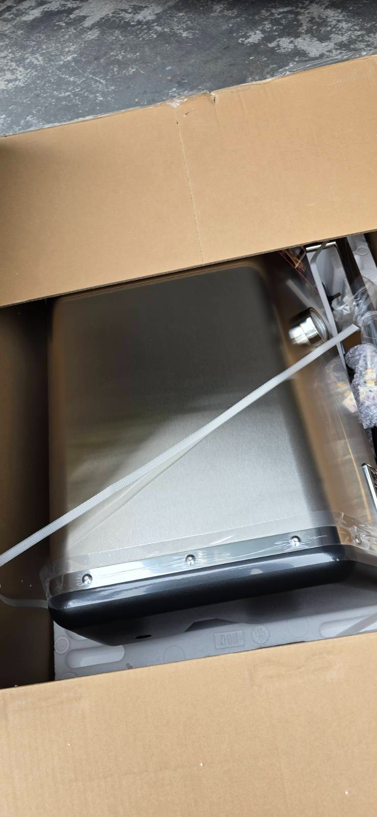 A rectangular object, possibly a water heater, inside a cardboard box.
