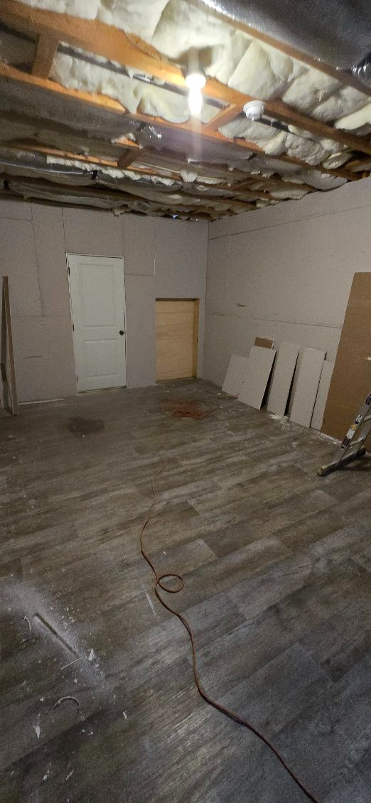 Room with damaged ceiling, worn wood floor, two doors, and some building materials.