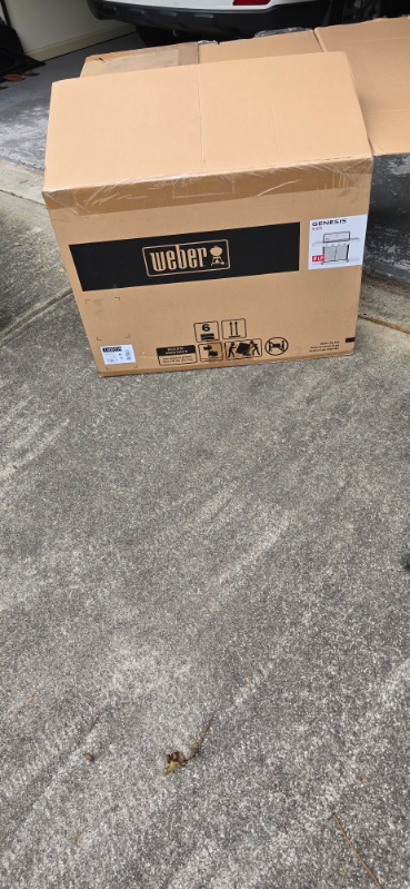 Cardboard box on a concrete surface, near a vehicle.